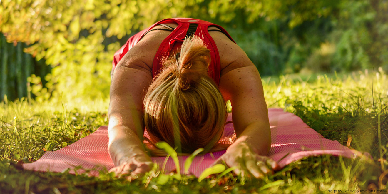 Frau kommt durch Yogastellung zur Ruhe, mitten im Grünen