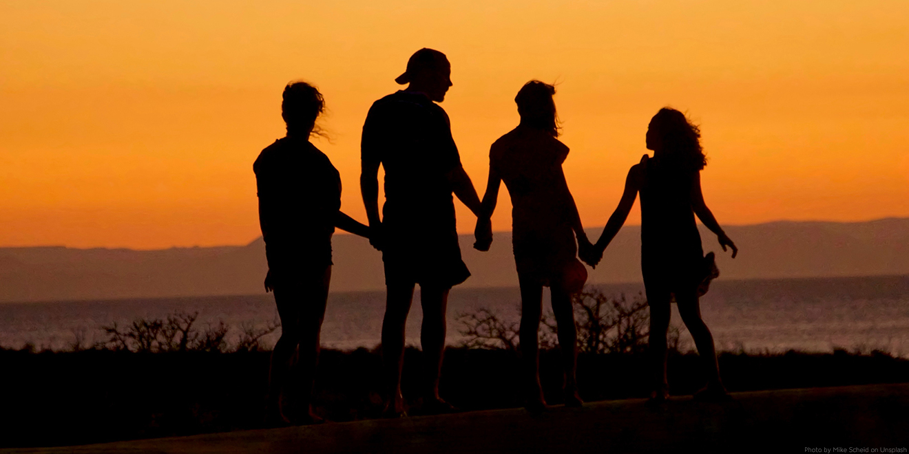 Familie steht gemeinsam am Sonnenuntergang und hebt die Hände. Eltern mit zwei Kindern. 