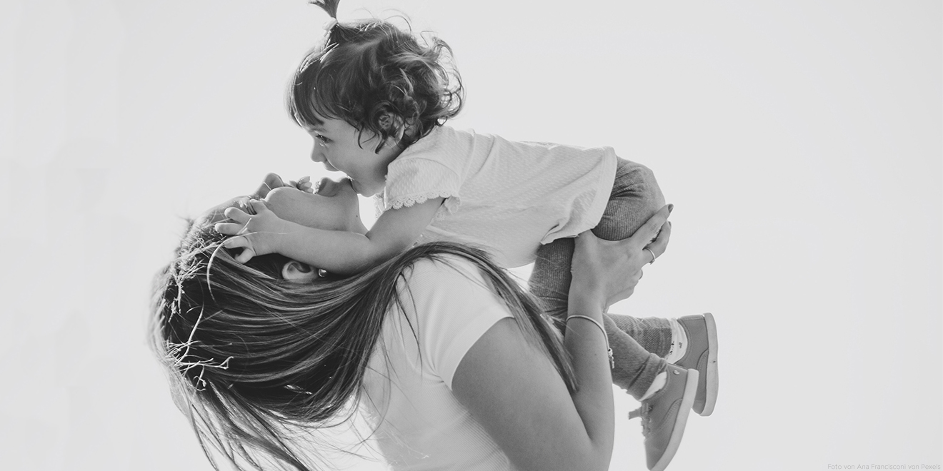 Mama lacht mit ihrer Tochter auf dem Arm. Sie machen Faxen und schenken sich gegenseitig viel Liebe. Genießt den Mutter- und Vatertag!