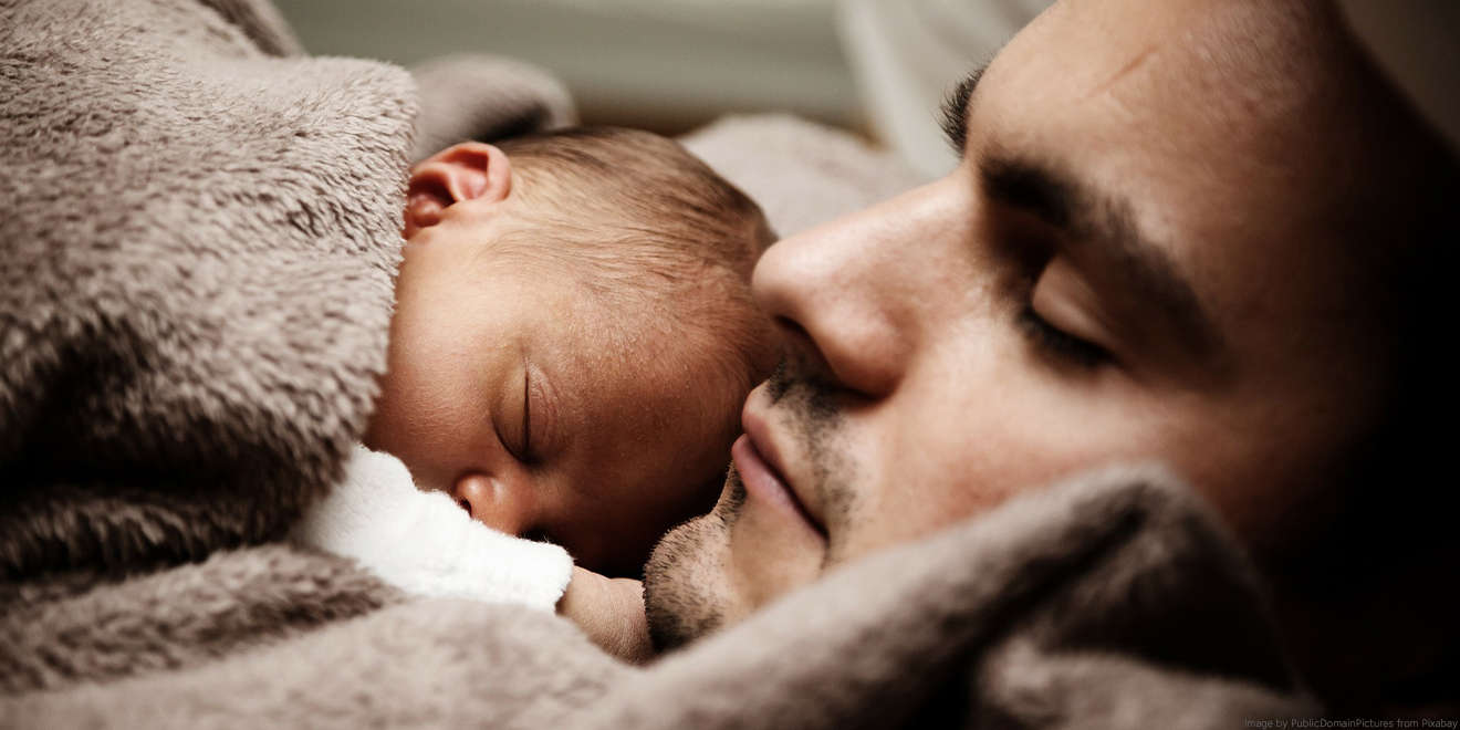 Papa kuschelt mit neugeboreneem Baby im Bett.