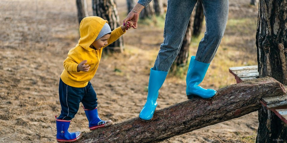 Mama hilft Kind über einen Baumstamm laufen. Soziale Selbstpflege bedeutet auch Persönlichkeitsentwicklung