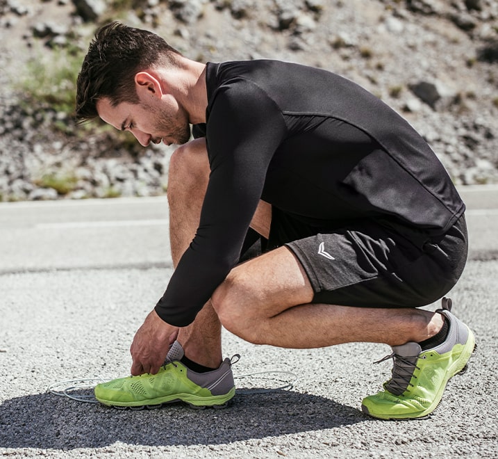 Herr mit Sportbekleidung schnürt sich die Schuhe um Joggen zu gehen. 