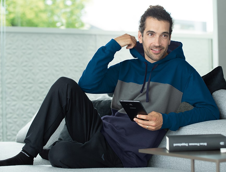 Oversize-Look stylen und mit Jogginshose kombinieren - Fertig ist das Loungewear Outfit für zuhause. Herr sitzt in lässigem Oversize-Hoodie im Wohnzimmer